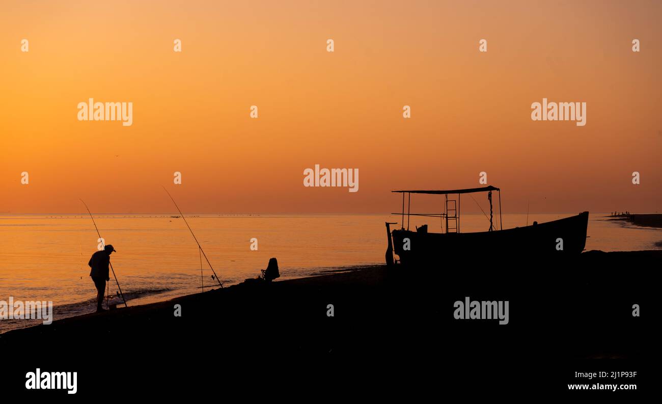 A fisherman with a fishing rod and a fishing boat on the seashore ...