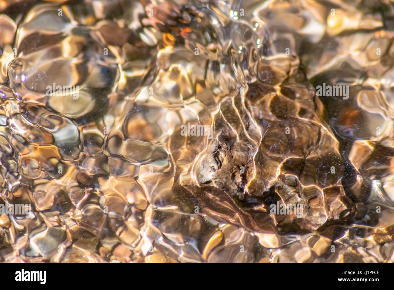 Stones in sparkling water with sunny reflections in water of crystal clear water creek as idyllic natural background shows zen meditation little waves Stock Photo