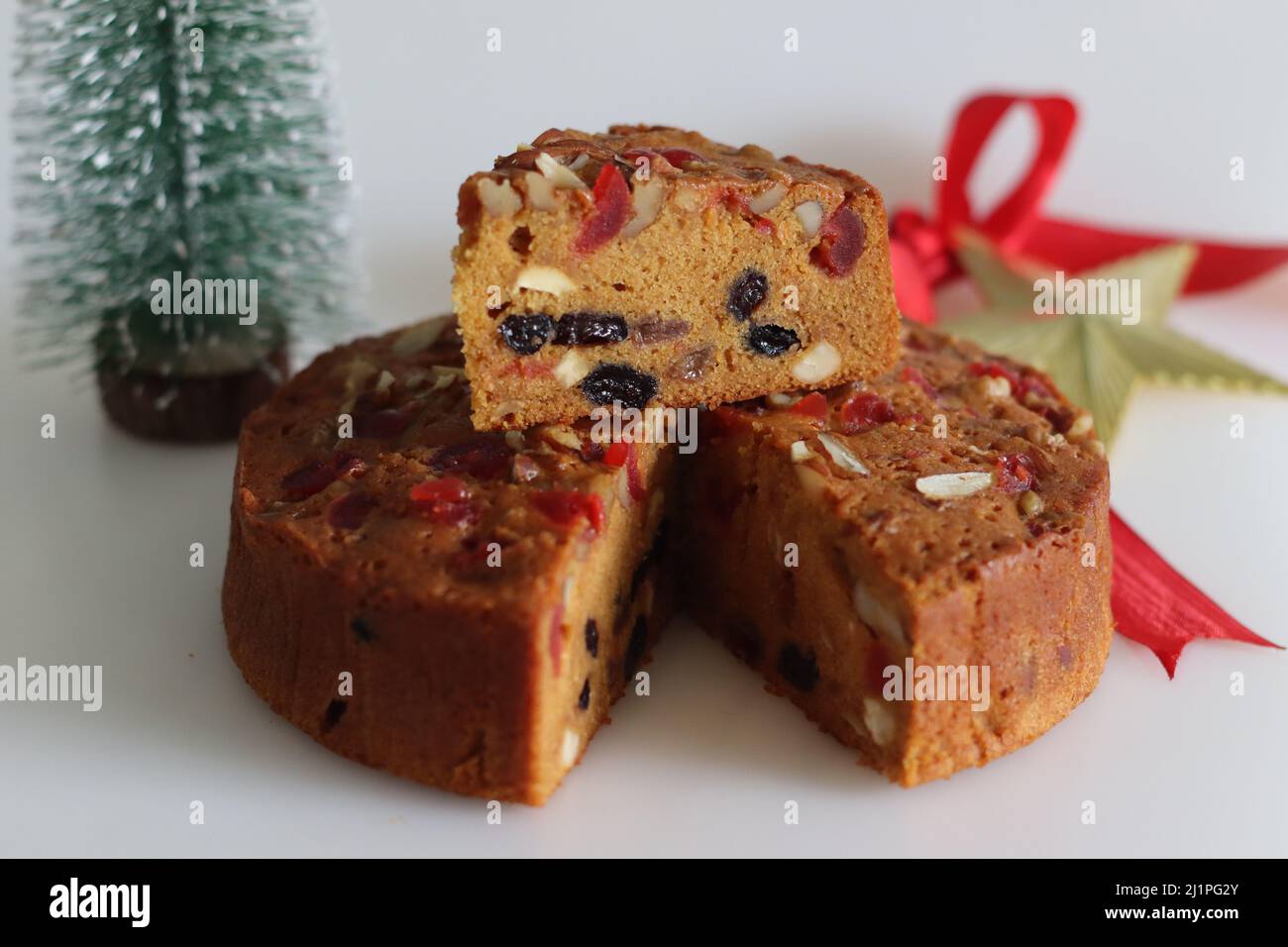 Sliced fruit cake with rum soaked fruits and nuts prepared for christmas. Shot with Christmas tree, pine corns, decorative ribbons in the background Stock Photo