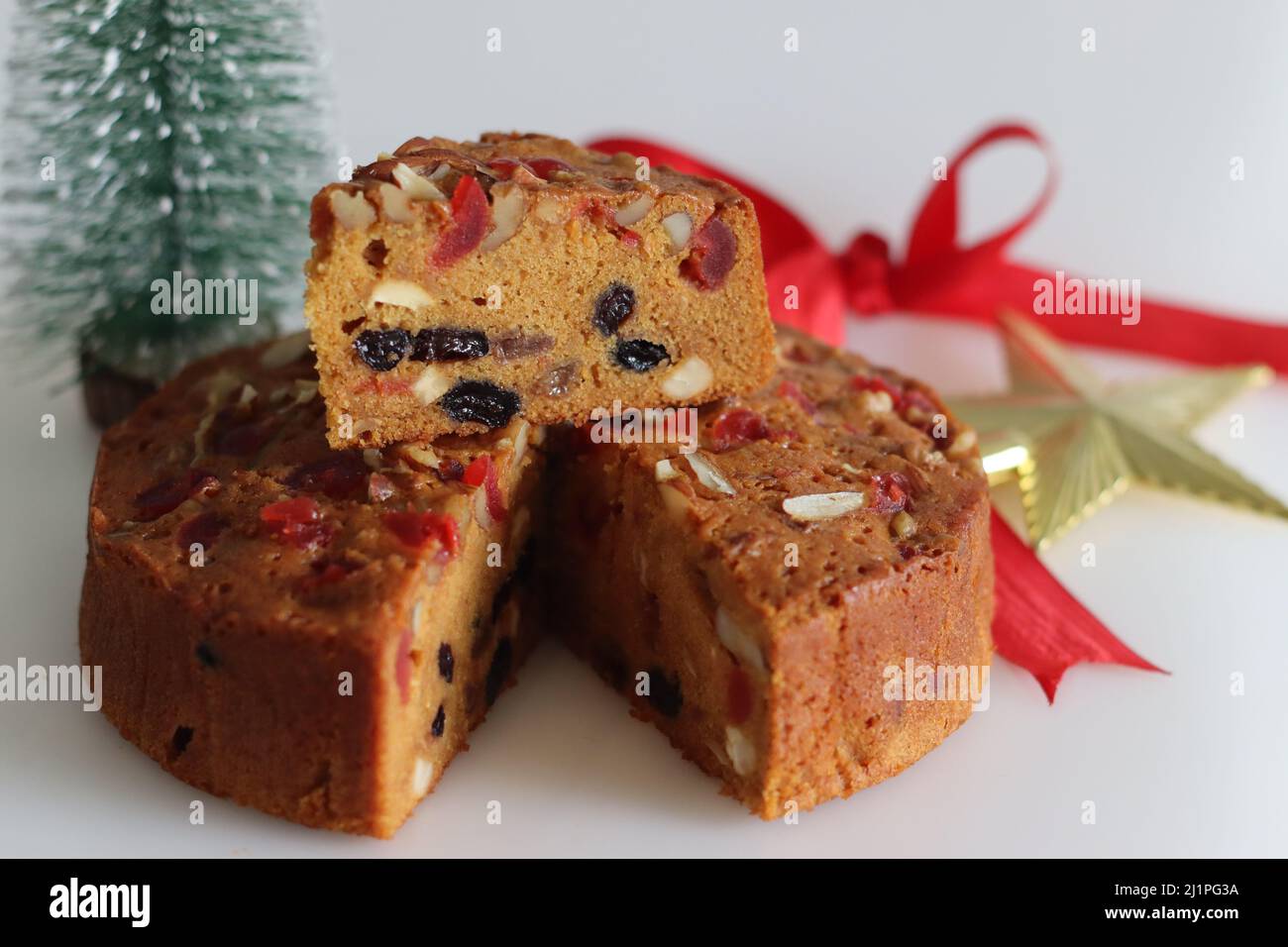 Sliced fruit cake with rum soaked fruits and nuts prepared for christmas. Shot with Christmas tree, pine corns, decorative ribbons in the background Stock Photo