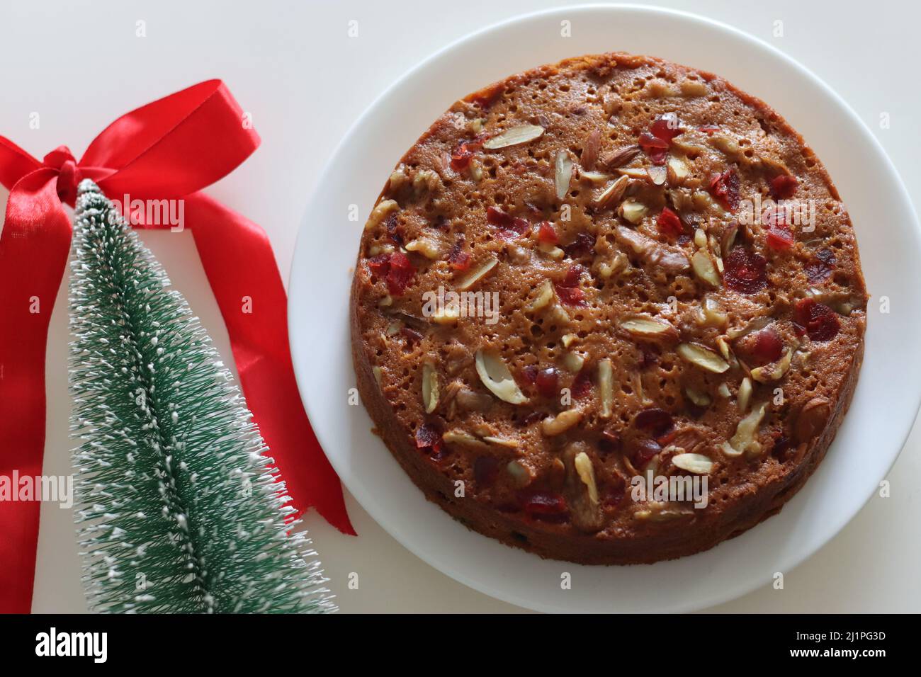 Fruit cake with rum soaked fruits and nuts prepared for christmas. Shot with Christmas tree, pine corns and decorative ribbons in the background Stock Photo