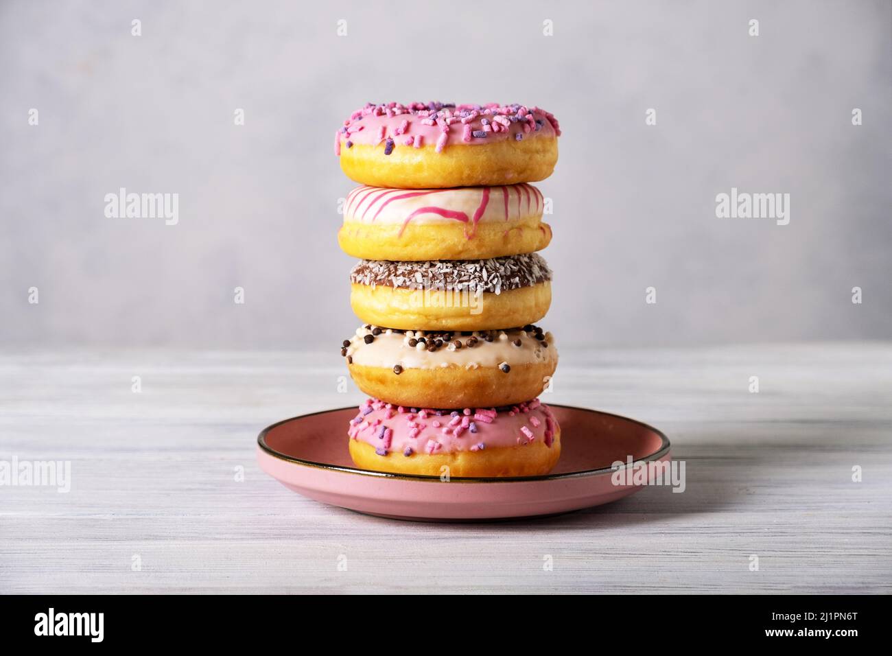 Stack of various colorful donuts on pink ceramic plate Stock Photo