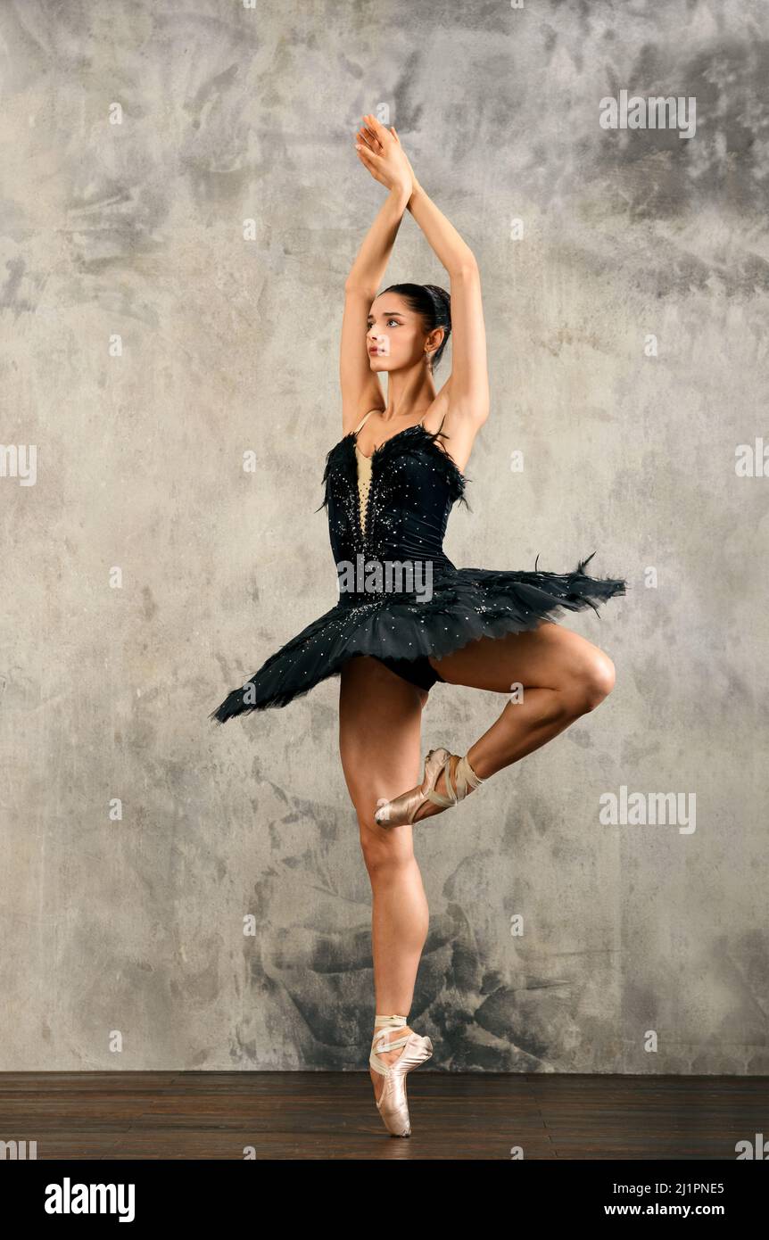 Graceful female ballet dancer in tutu skirt and pointe shoes balancing on leg and showing Passe position in dance hall Stock Photo