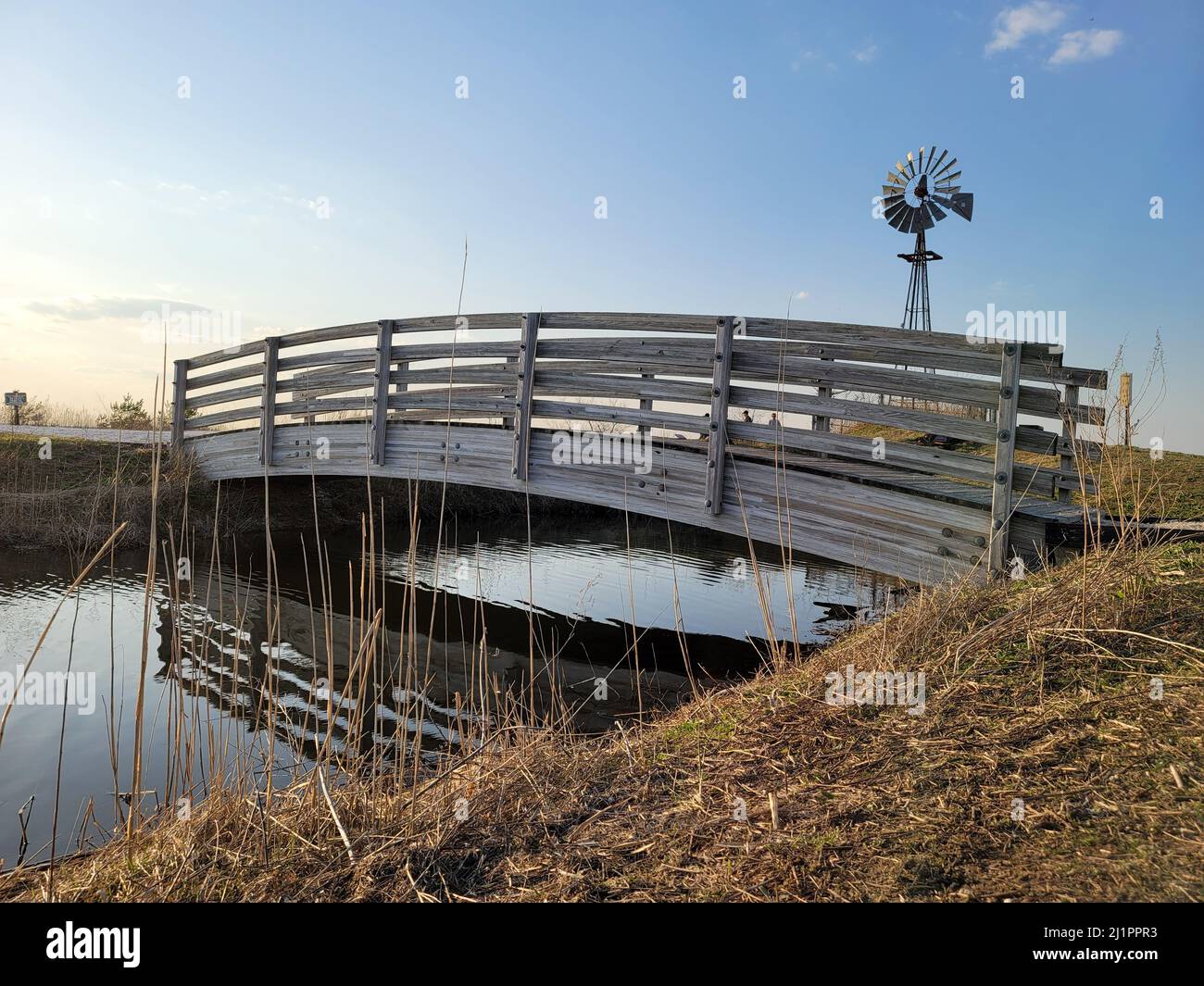 A wooden bridge over a small pond and a windmill in the background