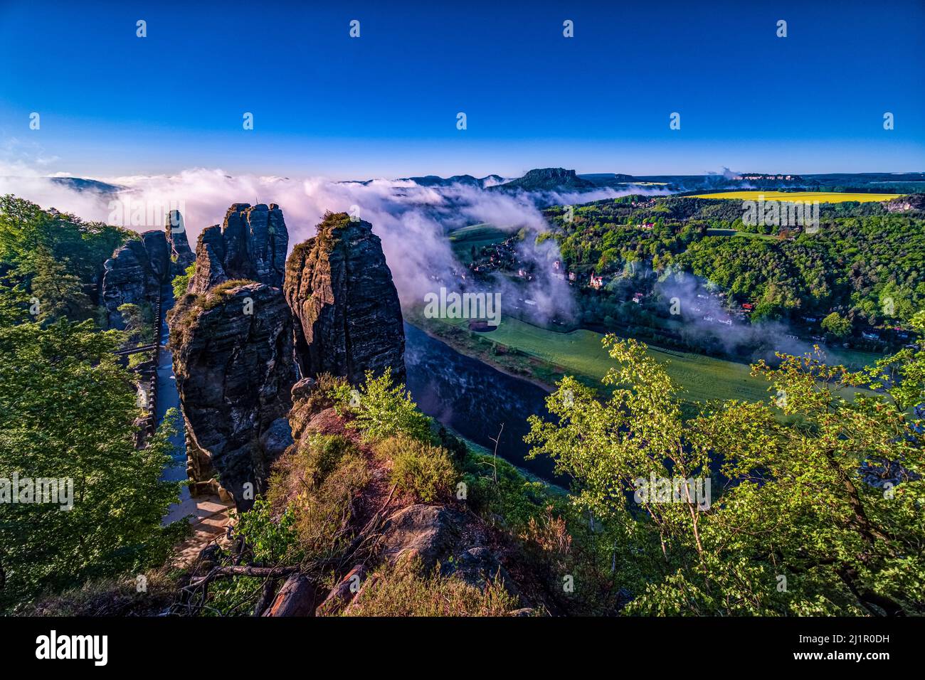 Landscape with the rock formation Bastei and the Elbe valley covered in fog in Rathen area of the Saxon Switzerland National Park at sunrise. Stock Photo