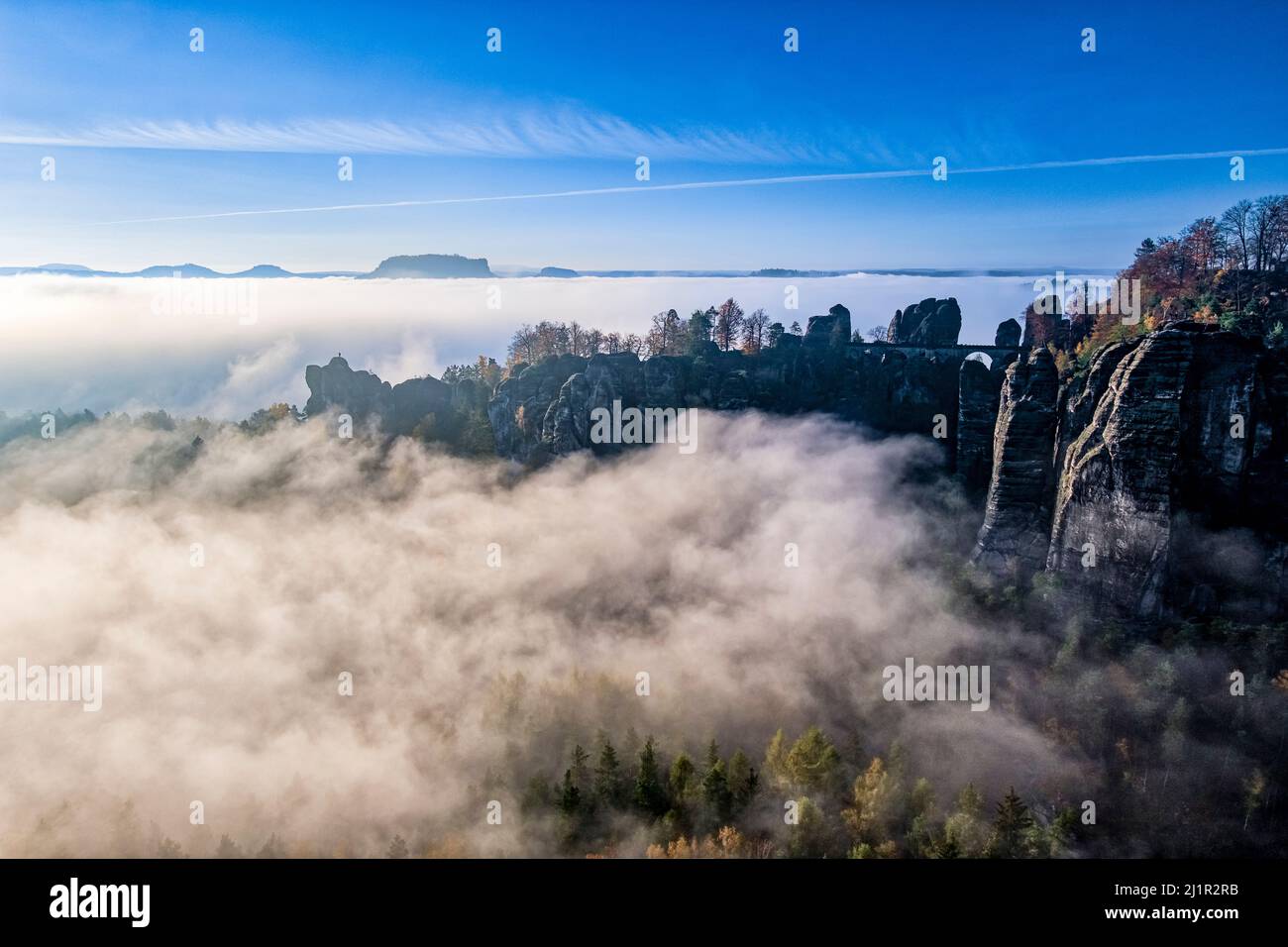 Landscape with the rock formations Felsenburg Neurathen and Bastei covered in fog in Rathen area of the Saxon Switzerland National Park in autumn. Stock Photo