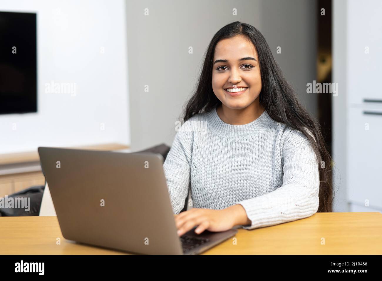 Beautiful and clever young middle eastern girl wearing casual clothes is using a laptop in cozy apartment, e-studying, working remotely Stock Photo
