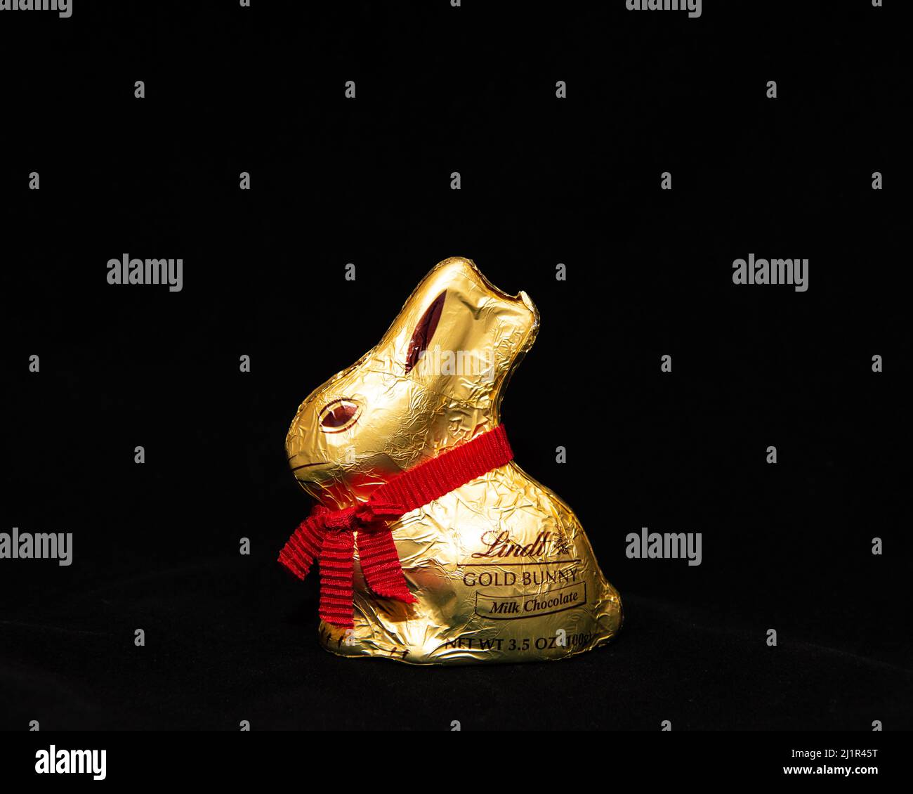 A milk chocolate Lindt Easter bunny wrapped in gold foil with a red ribbon necklace isolated on black Stock Photo
