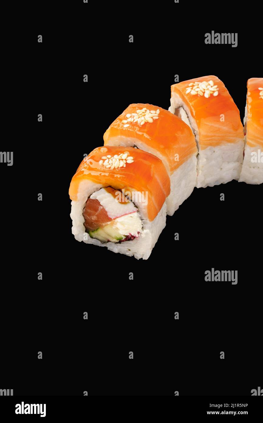 Sushi roll salmon, cold smoked salmon, Philadelphia cheese, snow crab, tobiko caviar, cucumber, unagi sauce, sesame seeds. Isolated on black backgroun Stock Photo