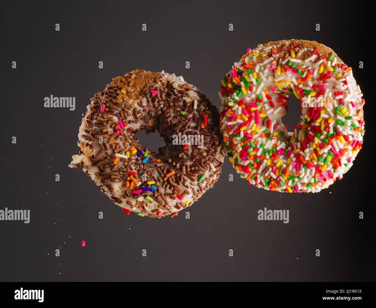 Two sweet colorful donuts in a frozen flight on a gray background. There are no people in the photo. There is free space to insert. Invitation for a h Stock Photo