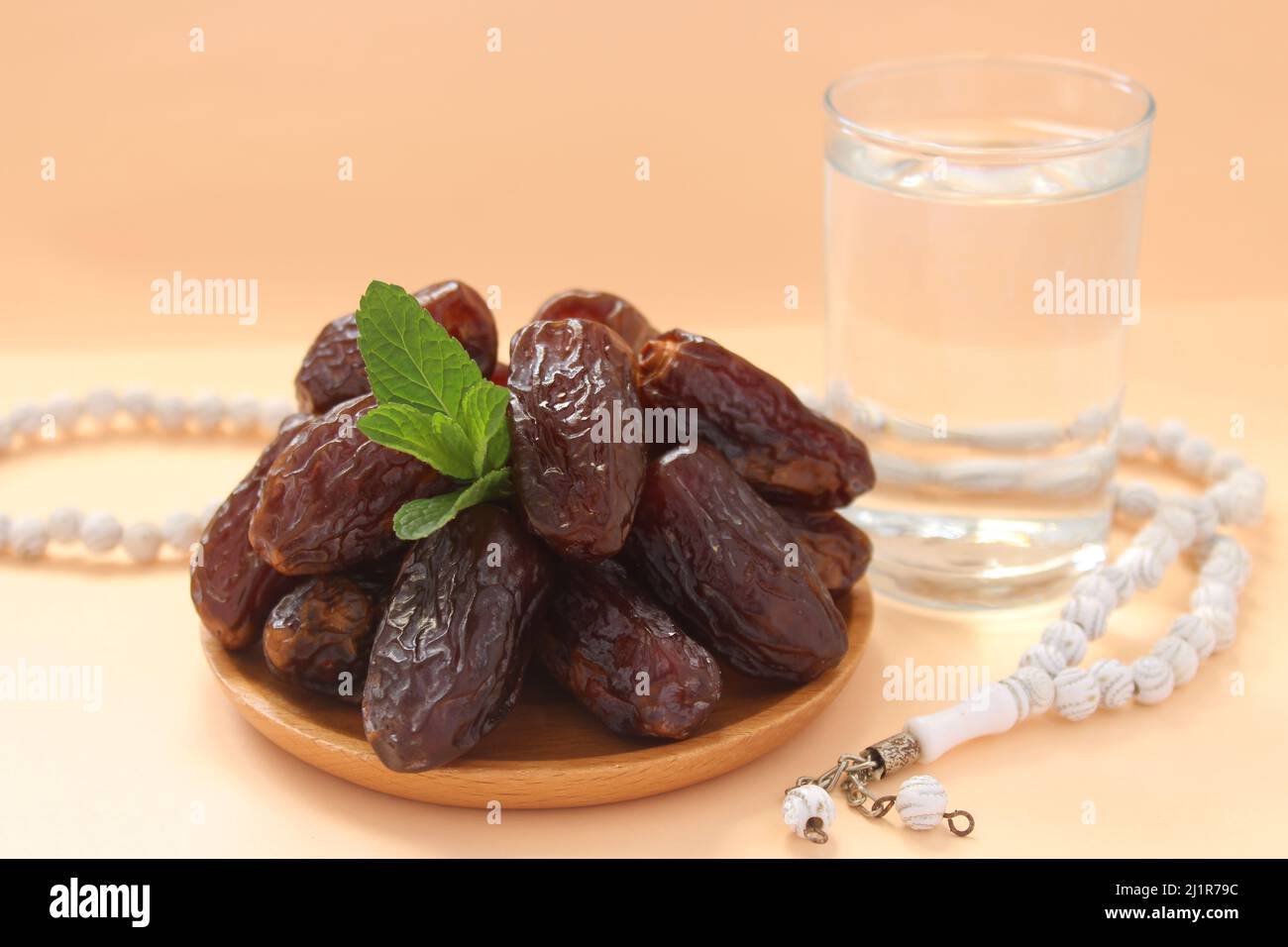 Date fruits in wooden plate, glass of water and white prayer beads. Fresh fruits for iftar. Ramadan concept idea photo. Stock Photo