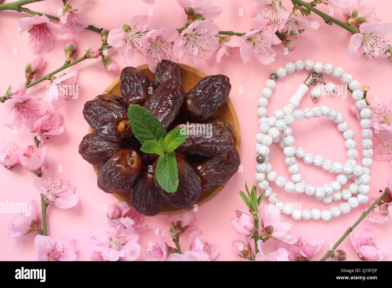 Date fruits in wooden plate and white prayer beads isolated on pink background. Ramadhan concept idea. flower frame. close up, top view. Stock Photo