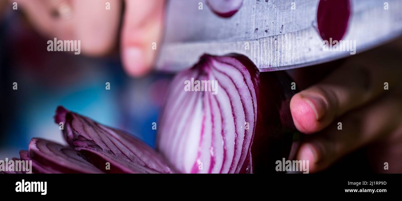 Women's hands cut a red onion with a big knife on a chopping board ...