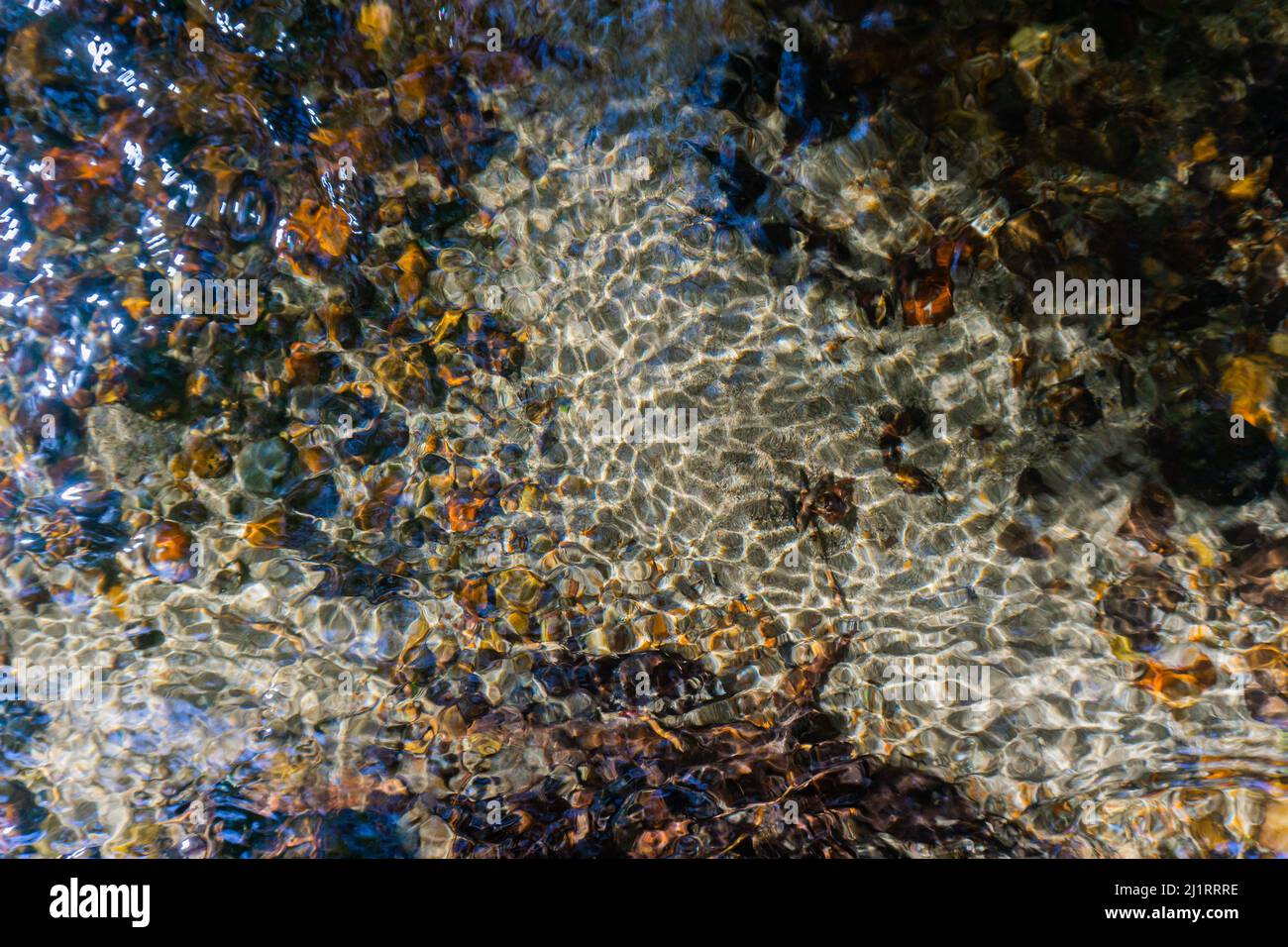 Texture on the bottom of a river featuring shiny waters and grey sand. Stock Photo