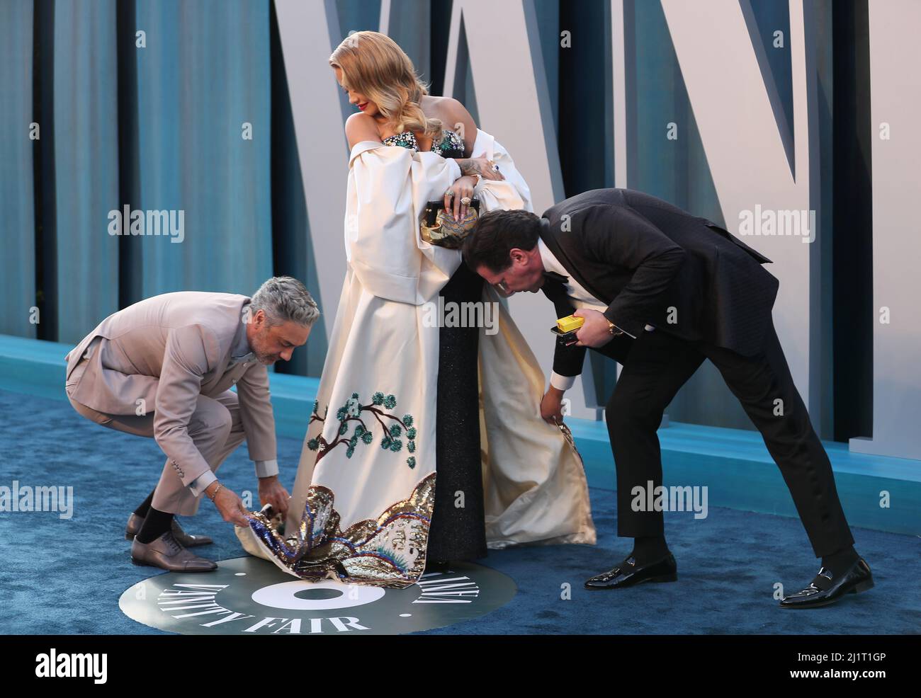 Taika Waititi (L) and a public relations professional adjust the dress of Rita Ora as they arrive at the Vanity Fair Oscar party during the 94th Academy Awards in Beverly Hills, California, U.S., March 27, 2022. REUTERS/Danny Moloshok Stock Photo