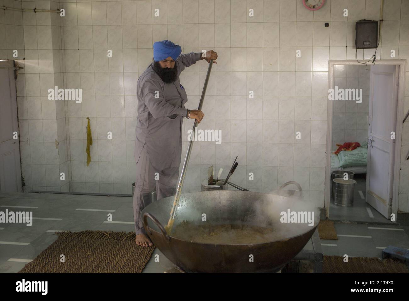 A Sikh man cooking in the free kitchen (Langar) of Gurdwara temple during daytime in New Delhi, India Stock Photo