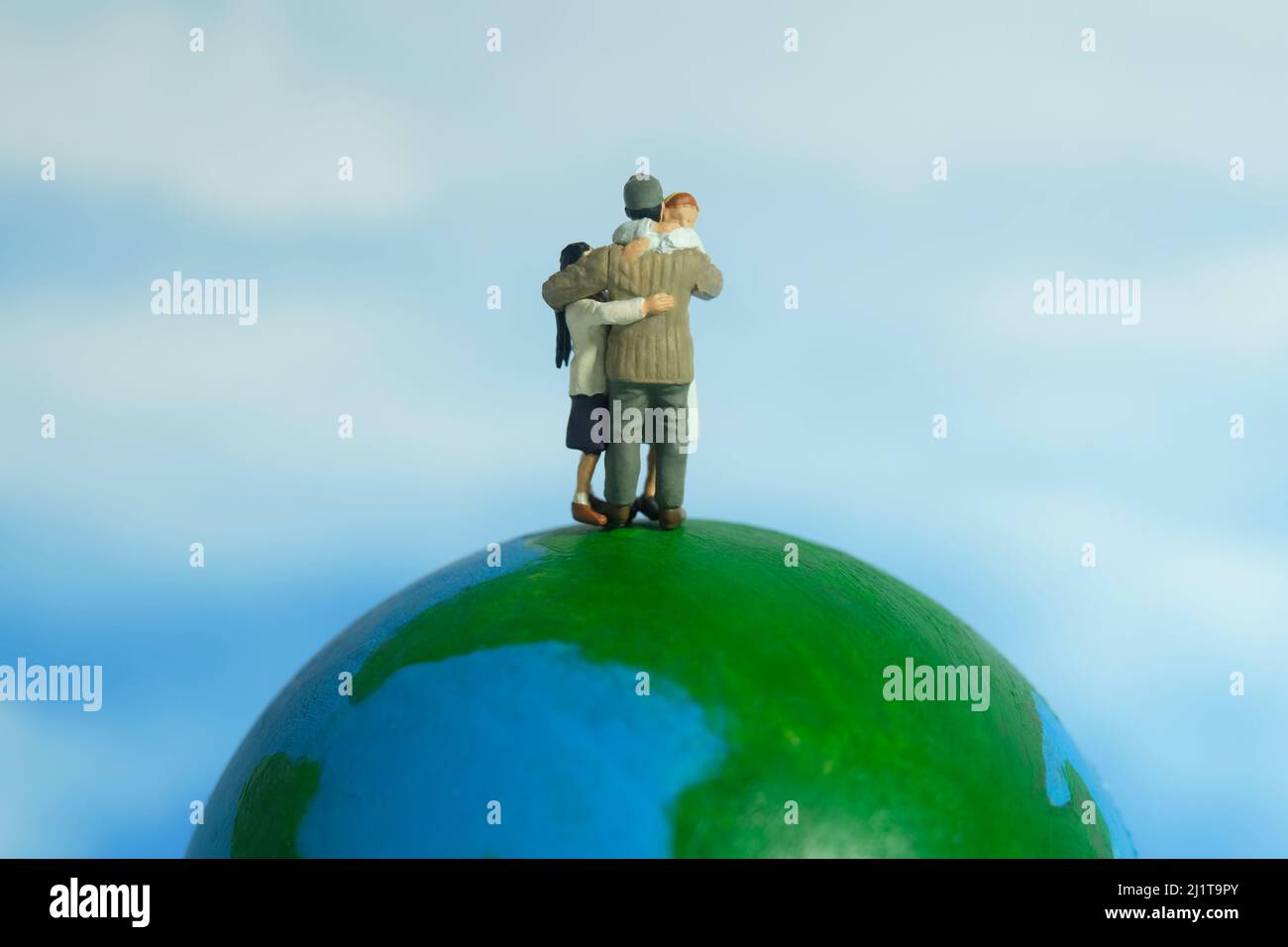 Miniature people toy figure photography. Family reunion day concept. Father hugging his wife and daughter above earth globe. Image photo Stock Photo