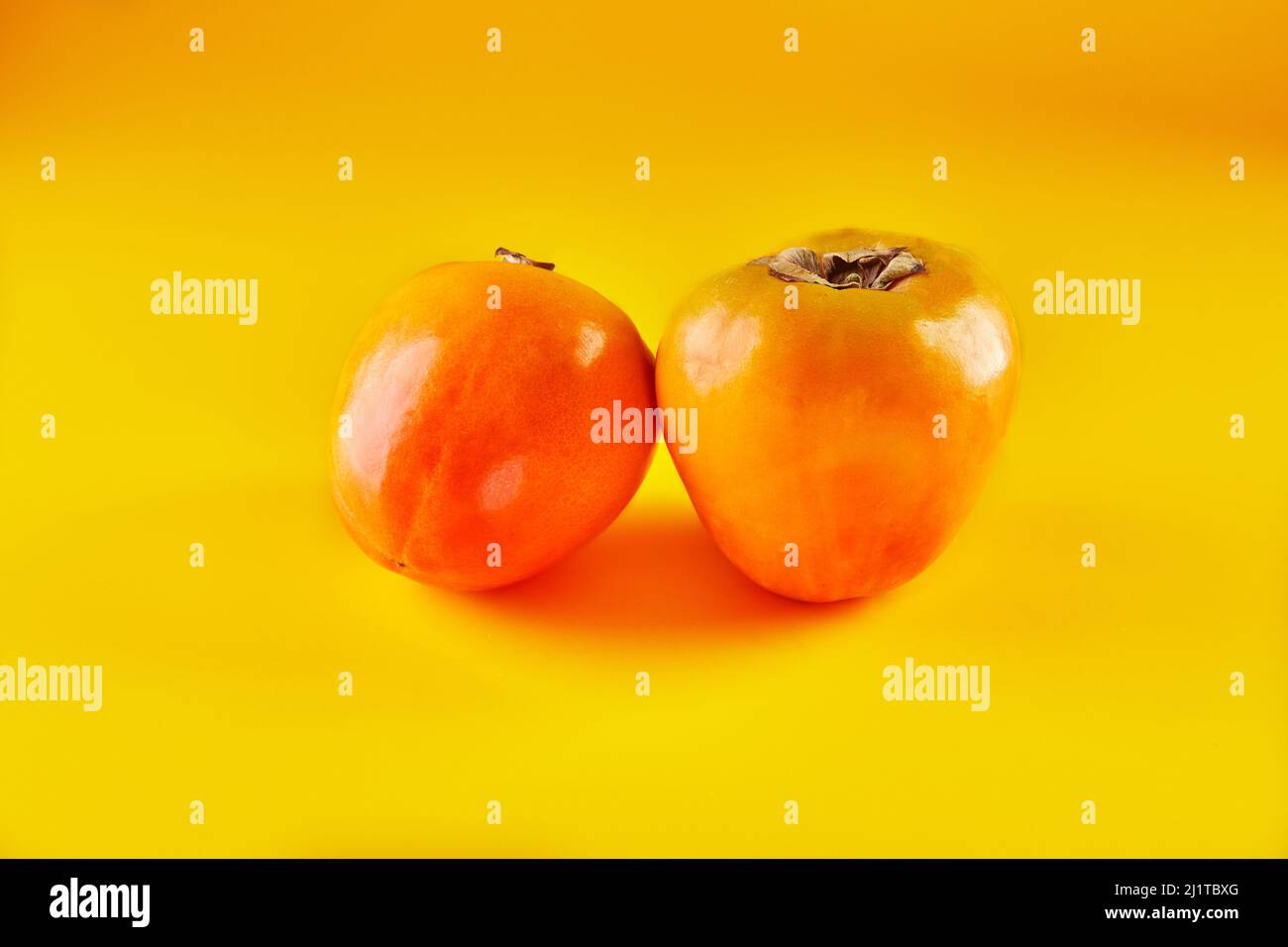 Two Persimmons isolated on yellow background in high resolution Stock Photo