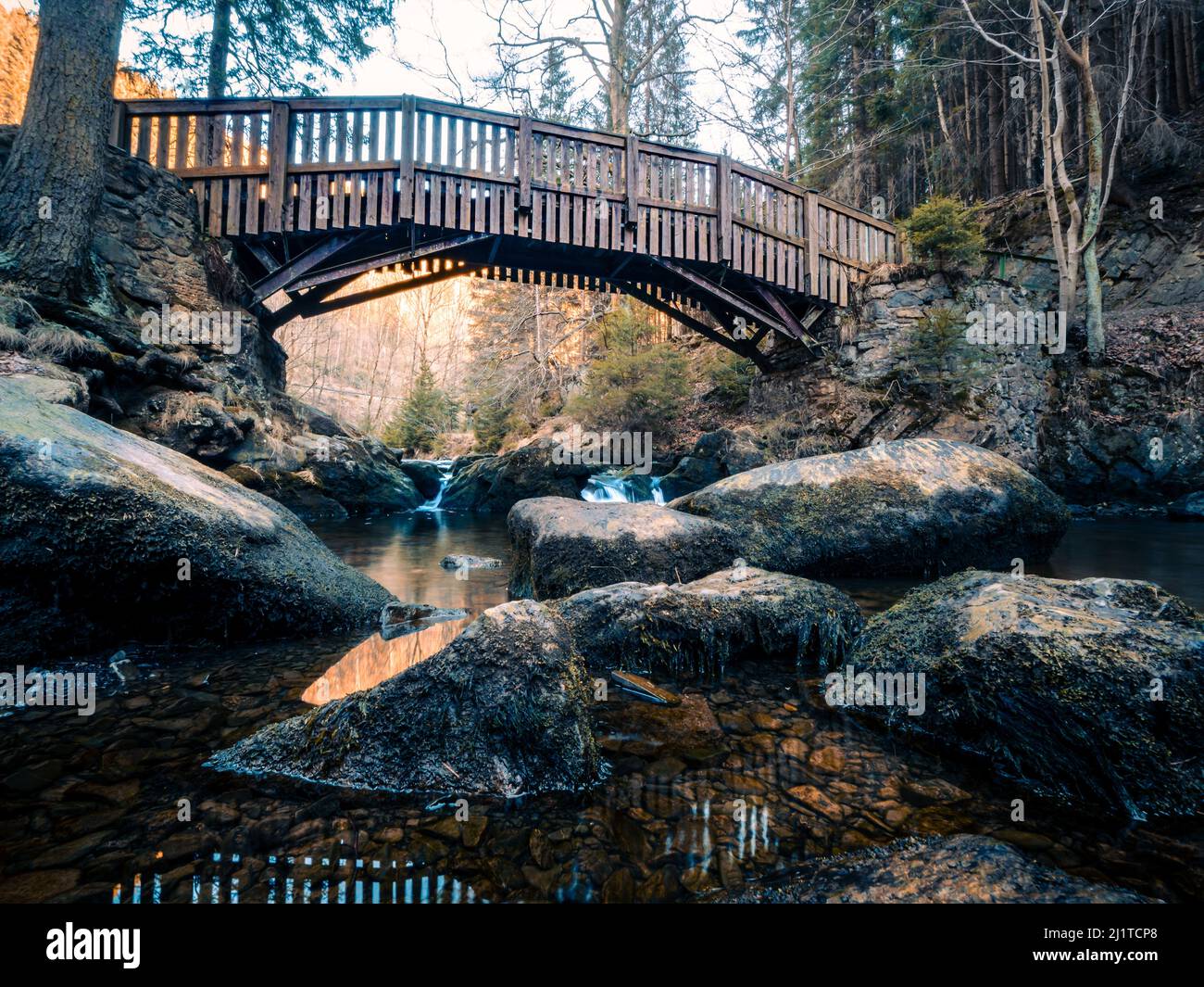 A beautiful shot of a wooden old bridge over a river with boulders in Verlobungsinsel, Okertal Harz, Germany Stock Photo