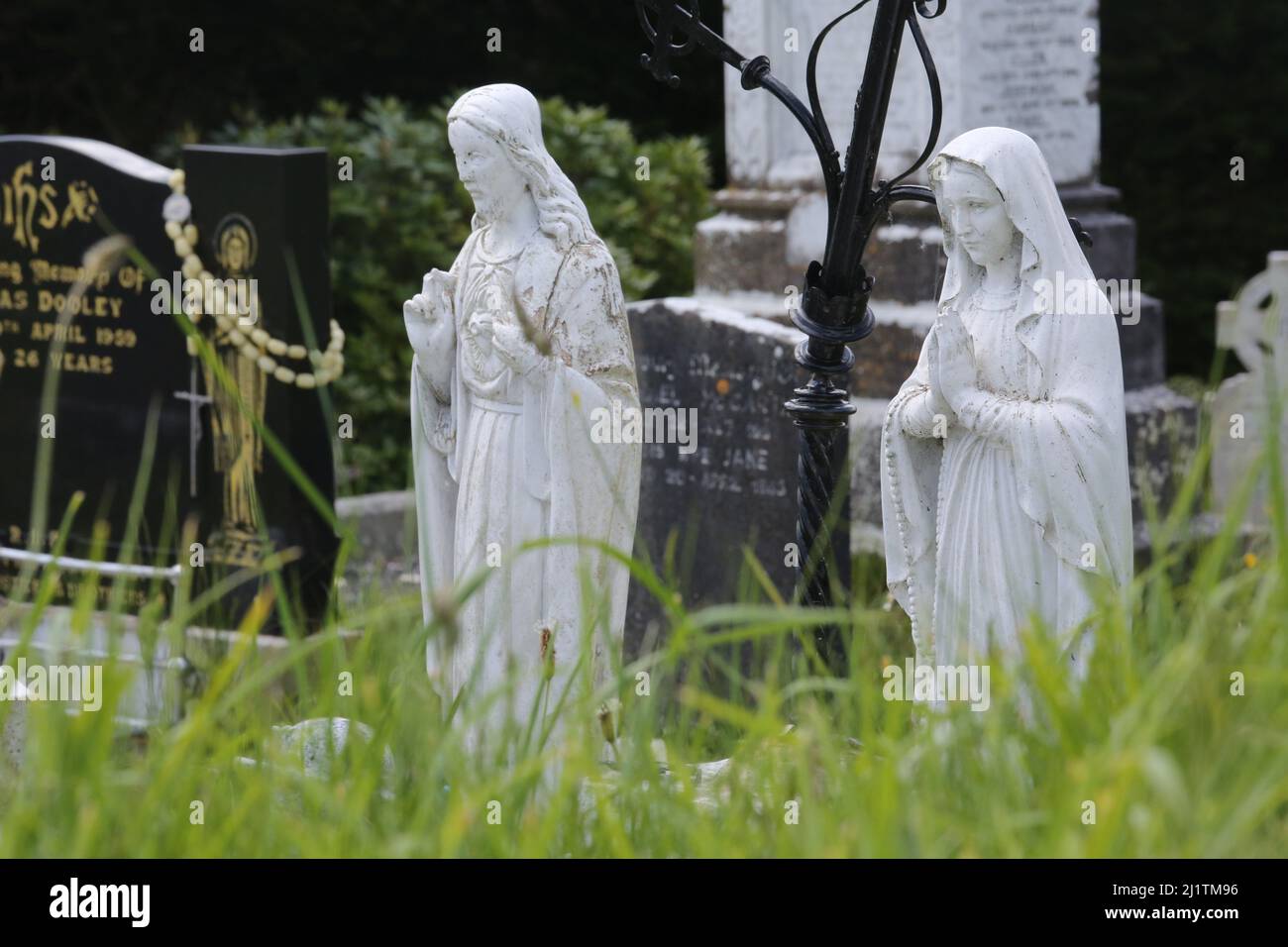 Religious statues in a cemetery in Ireland among other Catholic symbols including a Celtic cross. Stock Photo