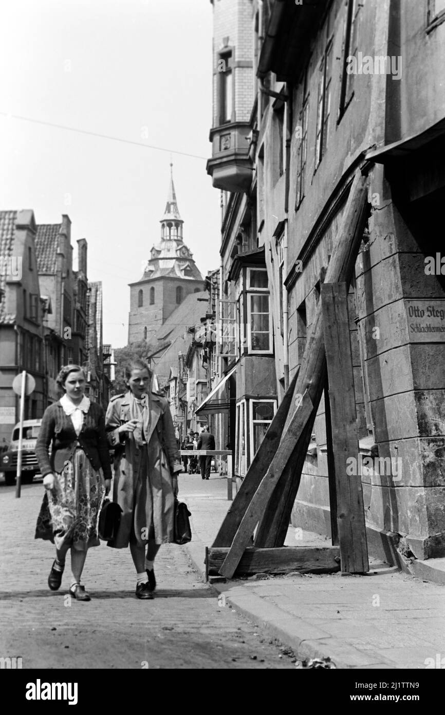 Frauen auf der Straße neben dürftig gestützter Hauswand, 1953. Women walking past a poorly supported house facade, 1953. Stock Photo