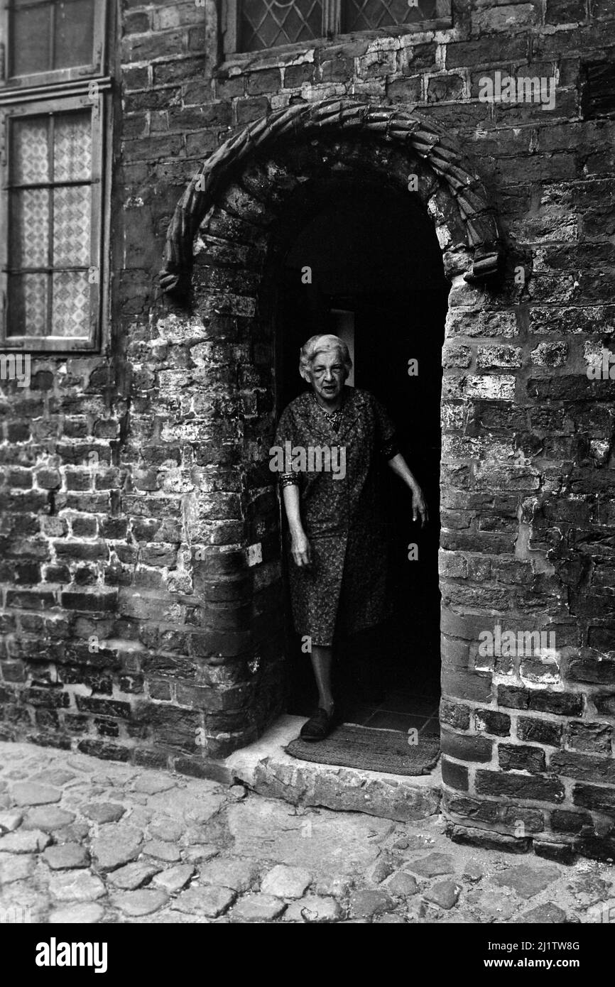 Seniorin auf der Türschwelle von Ziegelsteinbauten in Lüneburg, 1962. Elderly woman standing in the doorway of brick buildings in Lüneburg, 1962. Stock Photo