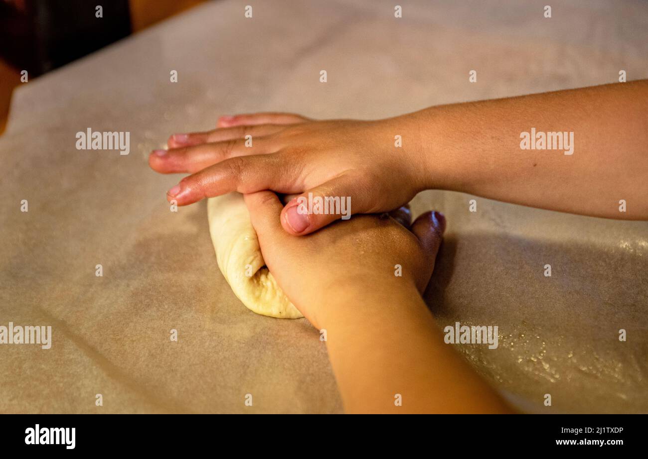 Child 's hands working fresh paste to make pasta on a pastry board. Boy or kid 's hand detail shaping dough. Learning cookery or bakery skills concept Stock Photo