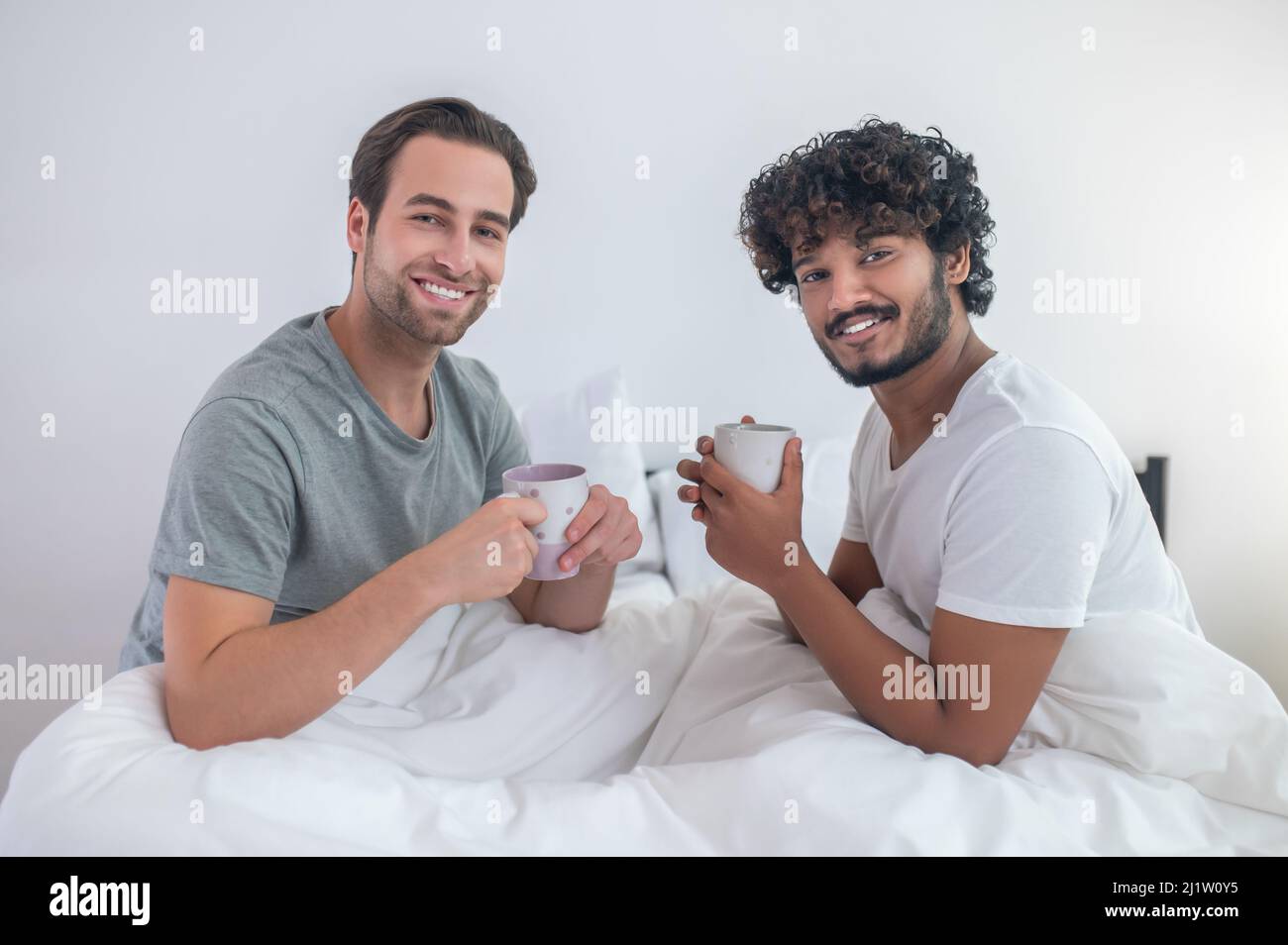 Happy gay couple drinking coffee in their bedroom Stock Photo