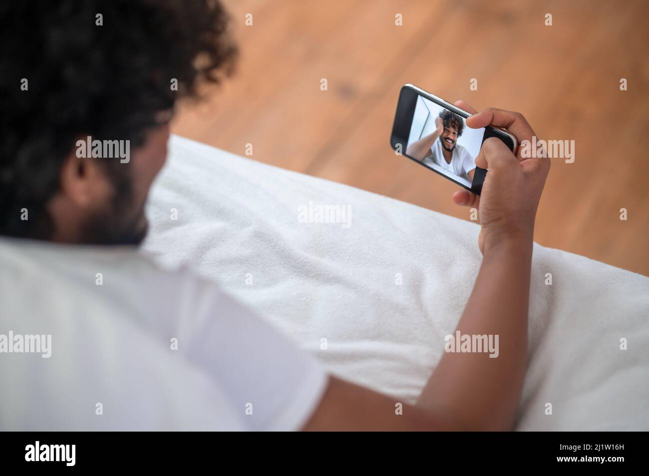 Curly-haired guy photographing himself with his cellphone Stock Photo
