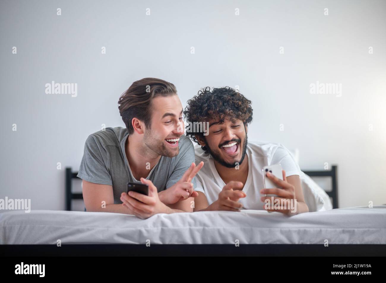 Joyful gay couple taking selfies in bed Stock Photo