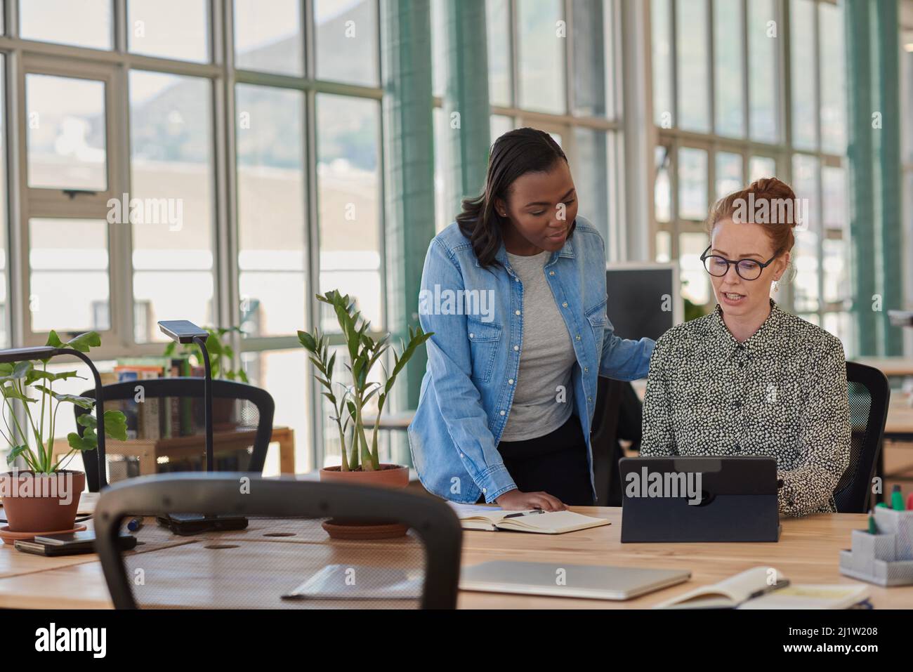 Two diverse businesswomen working on a tablet at an office desk Stock Photo