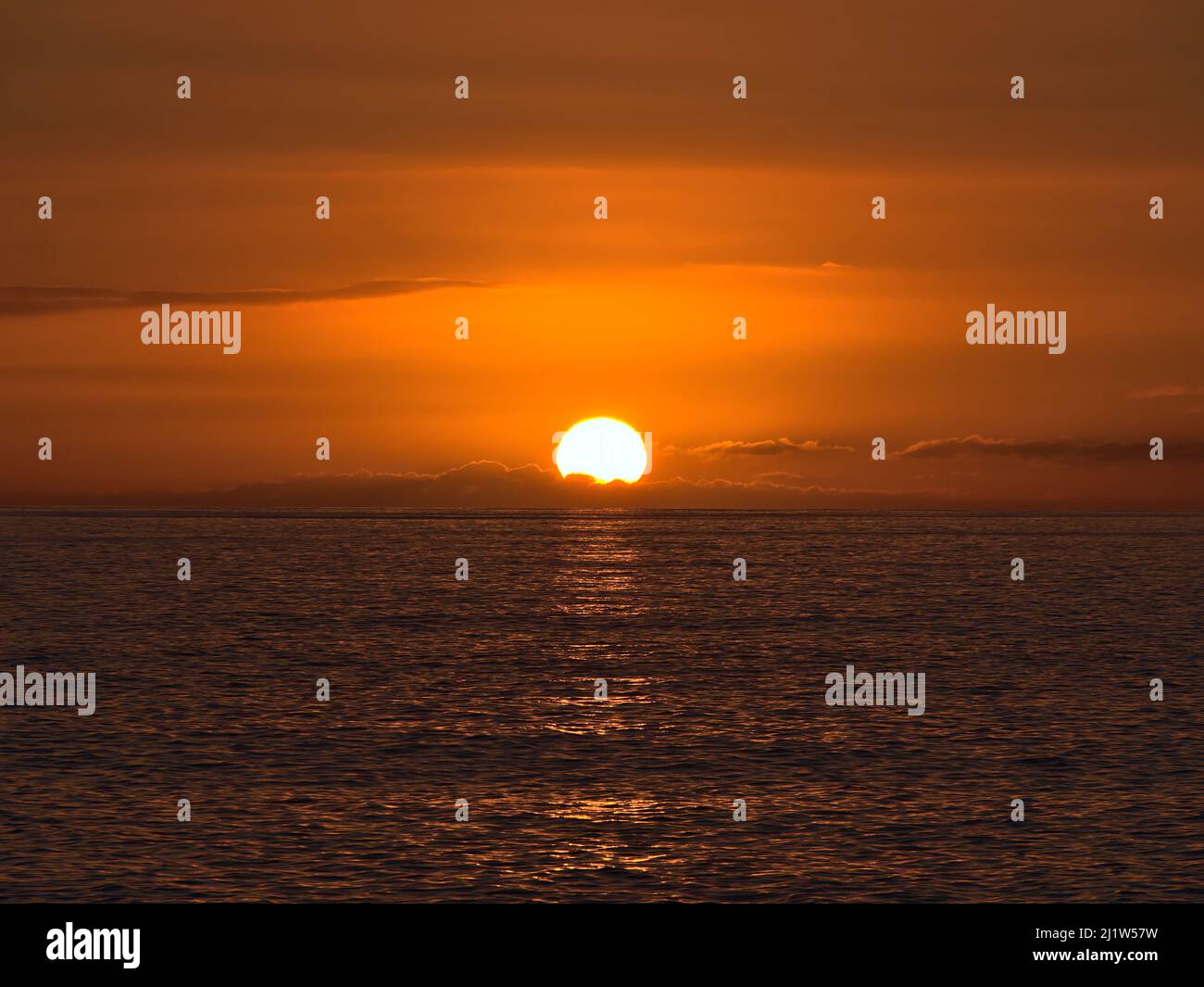 Sunset above the Atlantic Ocean with bright sun disappearing between low clouds on the horizon and orange sky viewed from the coast of Gran Canaria. Stock Photo