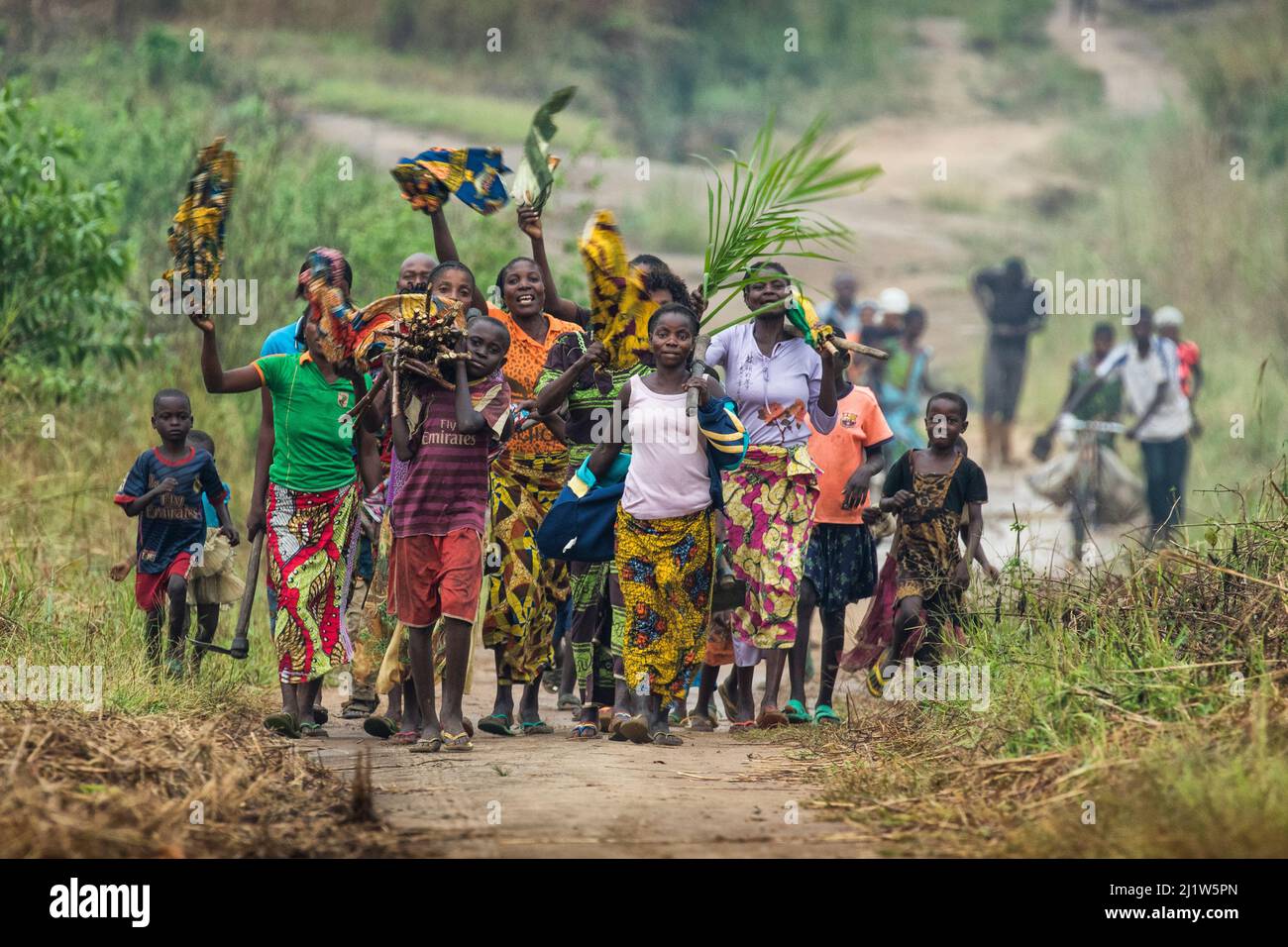 Women and children walking along road carrying fire wood and waving, Democratic Republic of Congo. May 2017. Stock Photo