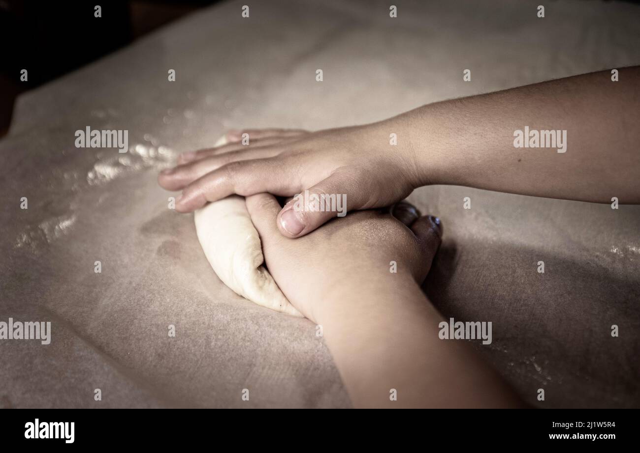 Child 's hands working fresh dough on a board. Boy or kid 's hand detail shaping paste conveys learning cooker illustration or bakery skills concept Stock Photo