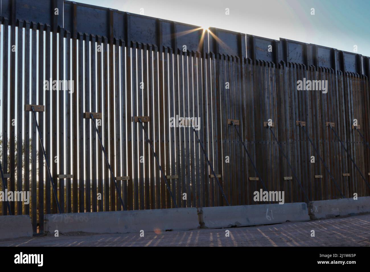 Border wall through Sonoran Desert, sun rays at top of wall. Organ Pipe Cactus National Monument