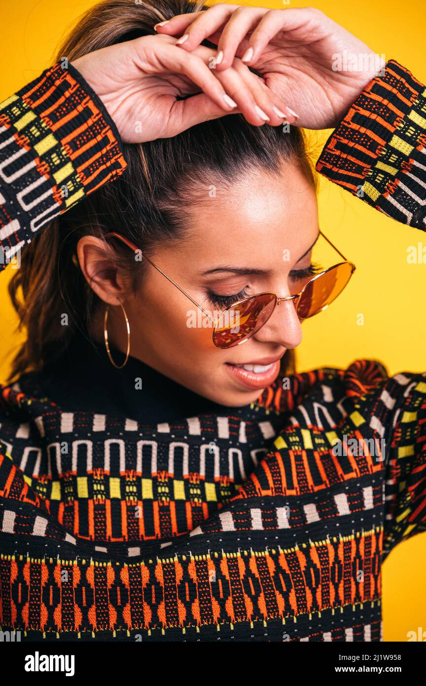 Headshot of smiling female model in trendy sunglasses and with ponytail on vivid yellow background in studio Stock Photo