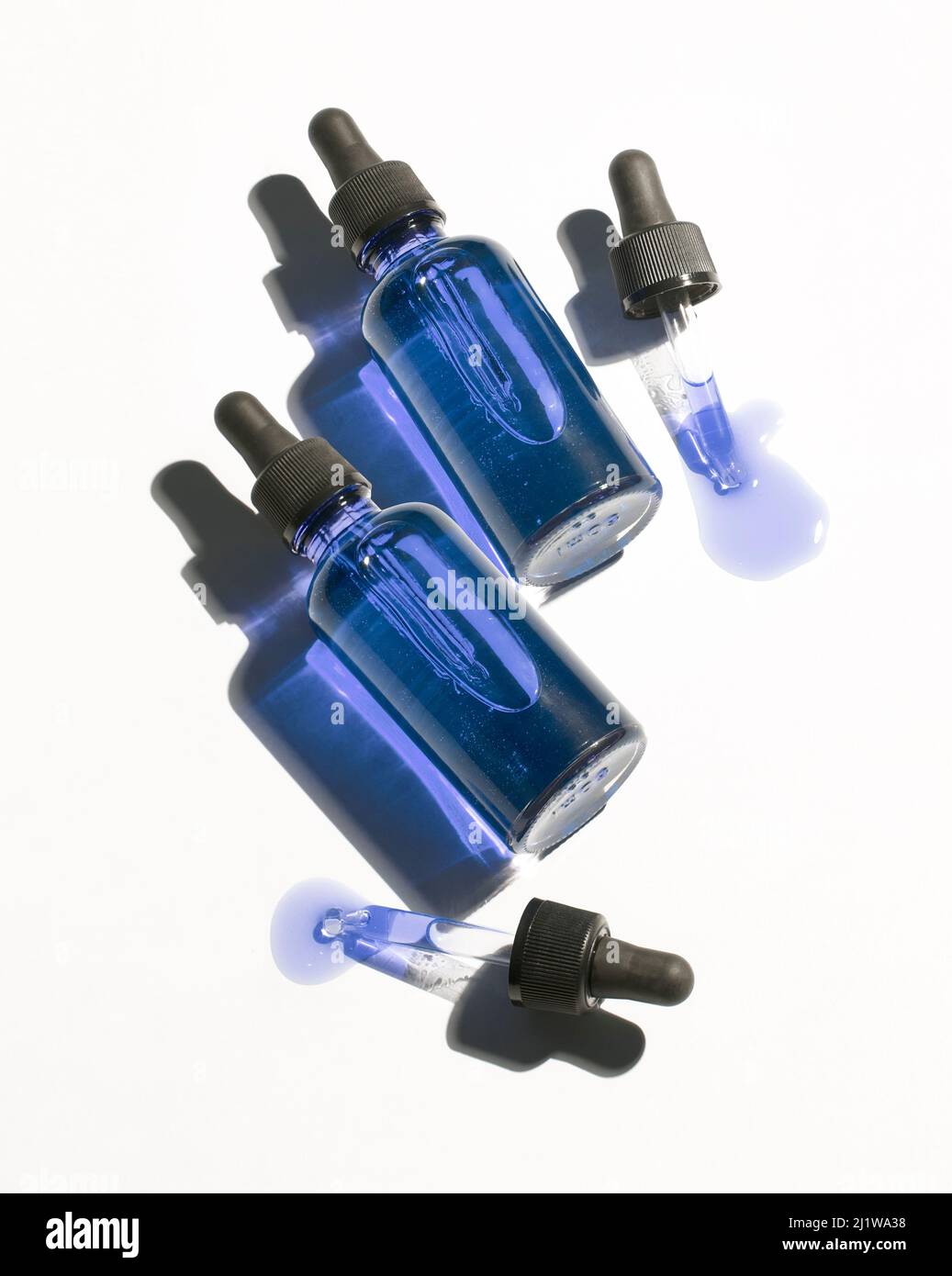 From above of glass bottles and pipettes with organic blue hyaluronic acid placed on clear white background in light room Stock Photo