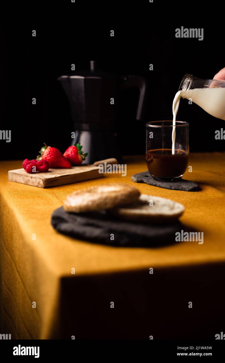 https://c8.alamy.com/comp/2J1WA5W/crop-anonymous-person-pouring-milk-from-jug-into-glass-cup-with-coffee-brewed-in-moka-pot-for-breakfast-with-strawberries-and-bagel-on-slate-plate-2J1WA5W.jpg
