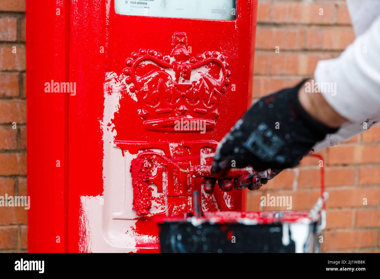 Wembley Park, UK. 28th March 2022.Royal Mails iconic red and black letterboxes get repaintd as part of their scheduled maintenance, approx. every 3 to 5 years. Having first applied a pink primer, within a few days, they are painted their traditional red and black colouring. Painter, Besim, has been repainting post boxes for 25 years. Amanda Rose/Alamy Live News Stock Photo