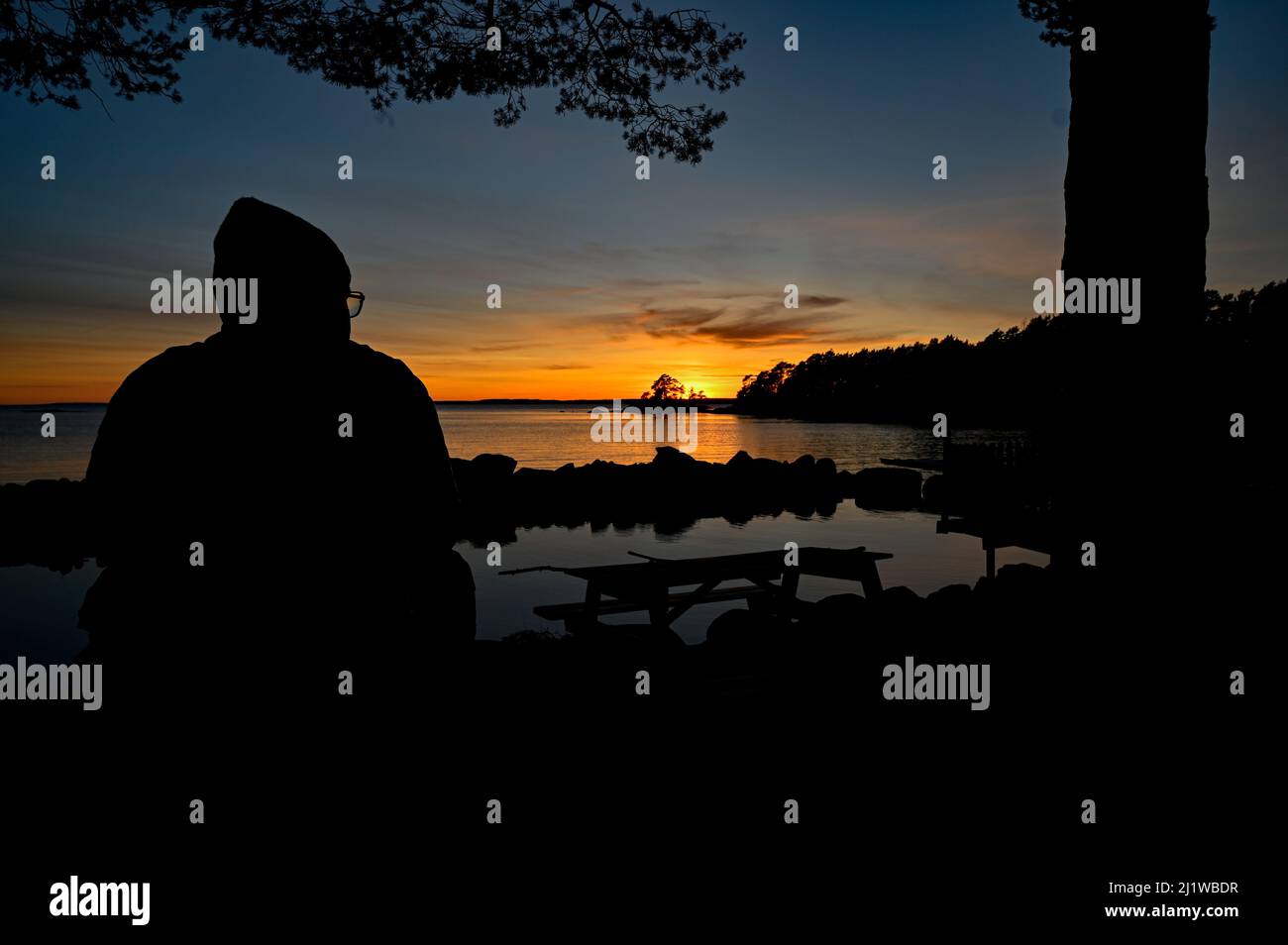 Man sitting overlooking sunset over lake Vattern Stock Photo