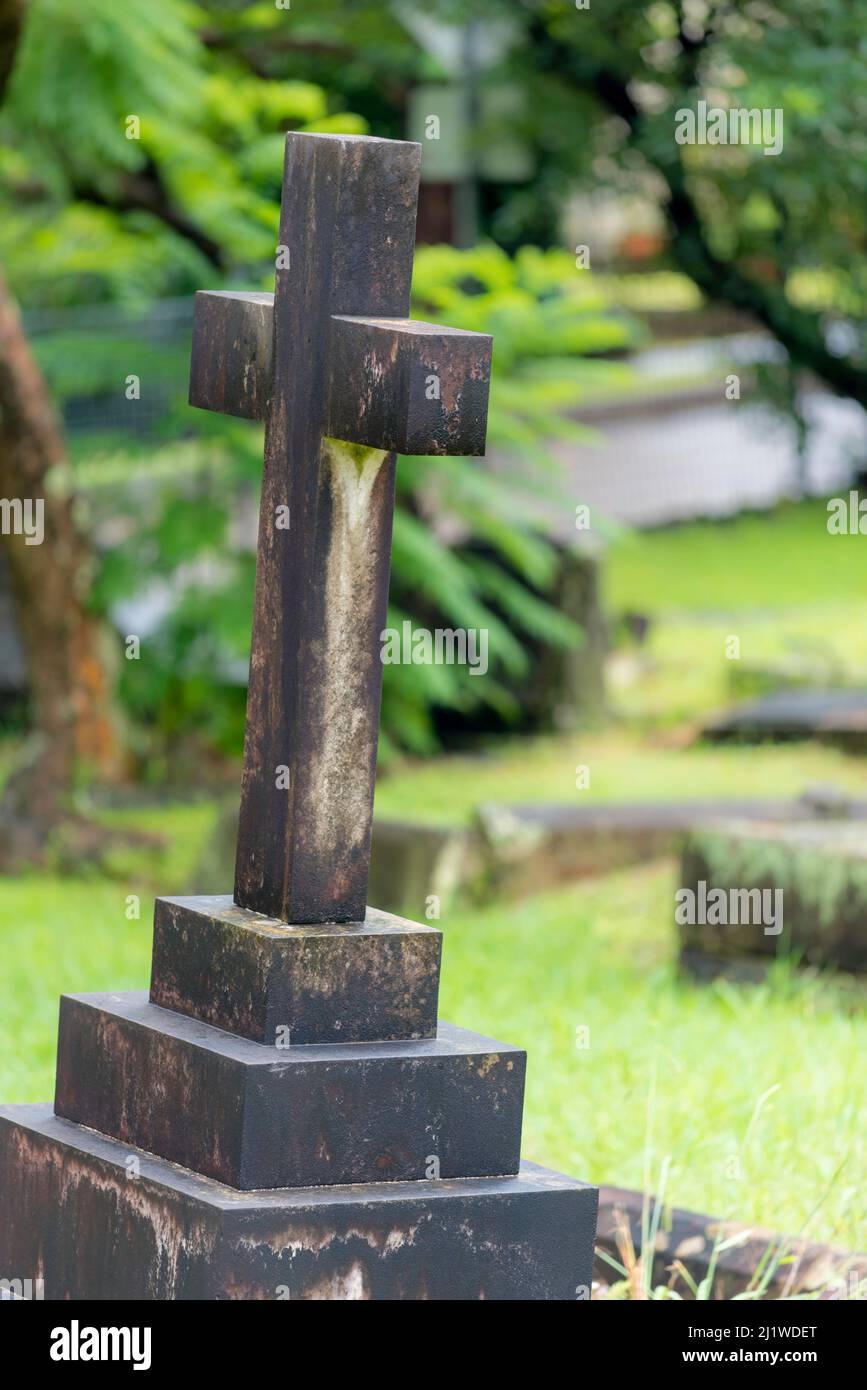 A from behind image of a stone or concrete cross near other graves, in