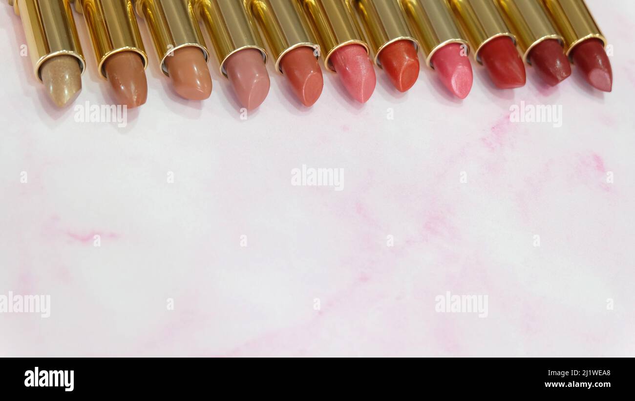 Lipsticks in different hues of red lined up side by side, on a pink marble background. With copy space on the bottom part. Stock Photo