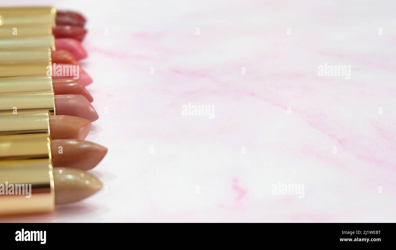 Lipsticks in different hues of red lined up side by side, on a pink marble background. With copy space on the right. Stock Photo