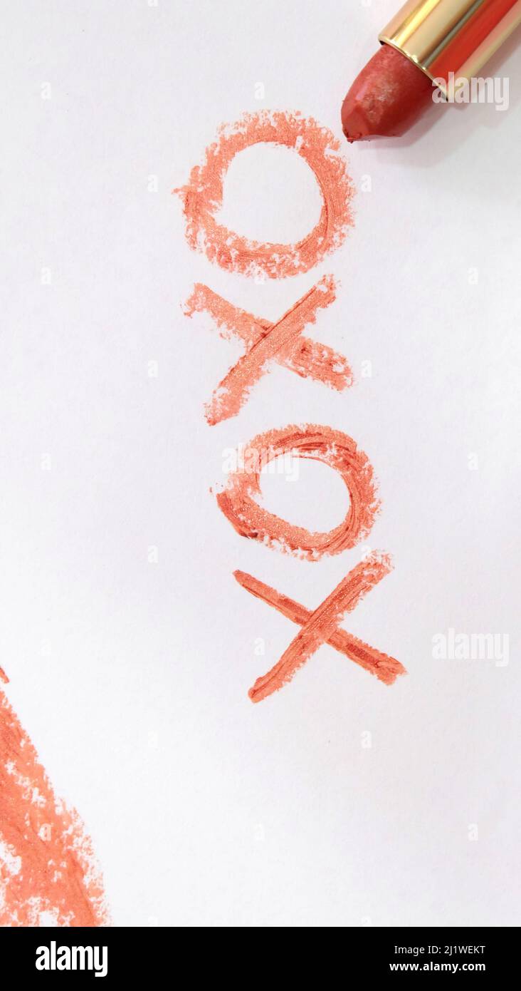 The symbol 'XOXO' written on a piece of paper with red lipstick, with the lipstick tube placed next to the word. Stock Photo
