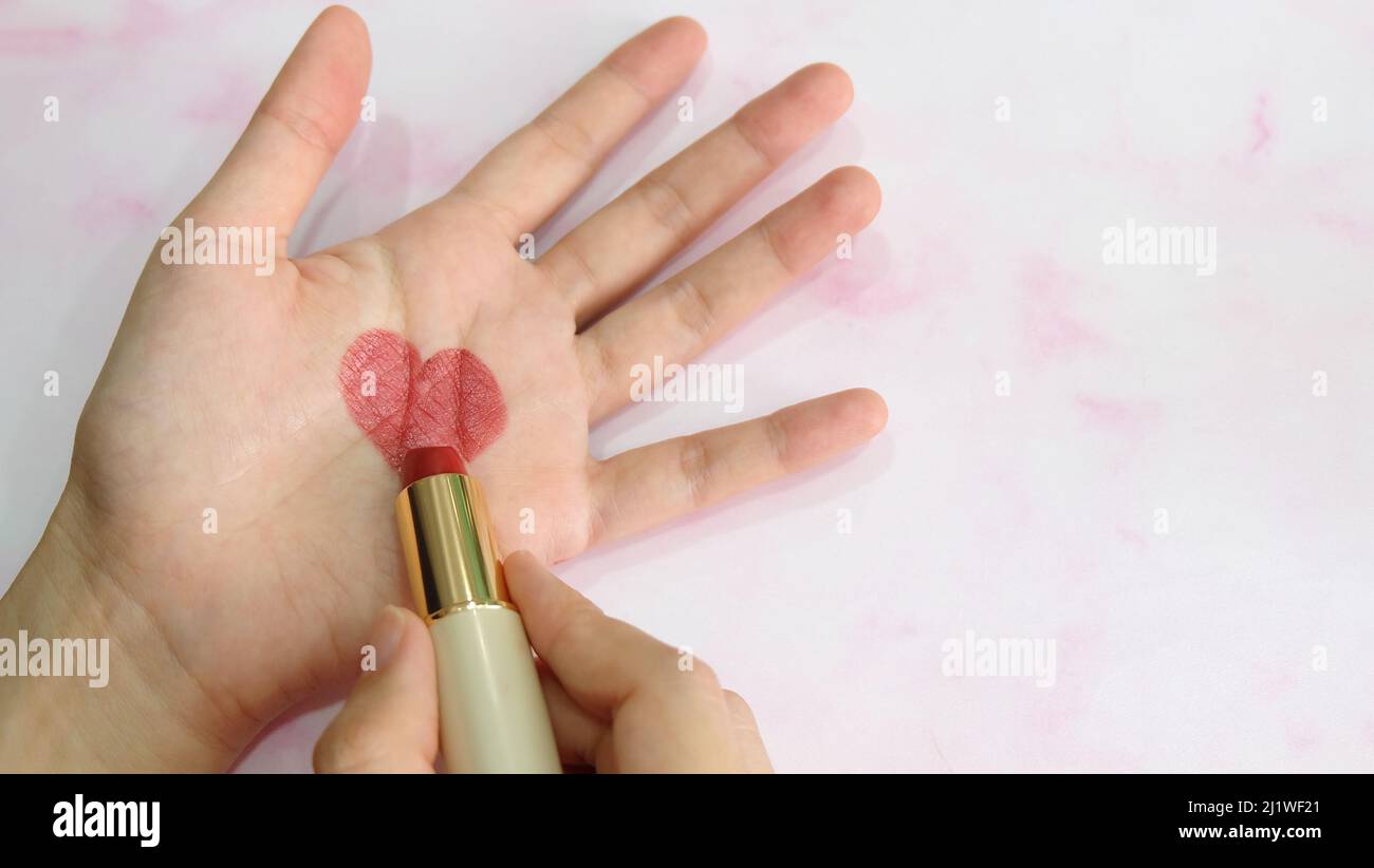 Hand holding a tube of lipstick, drawing a heart shape in the center of a palm. Stock Photo