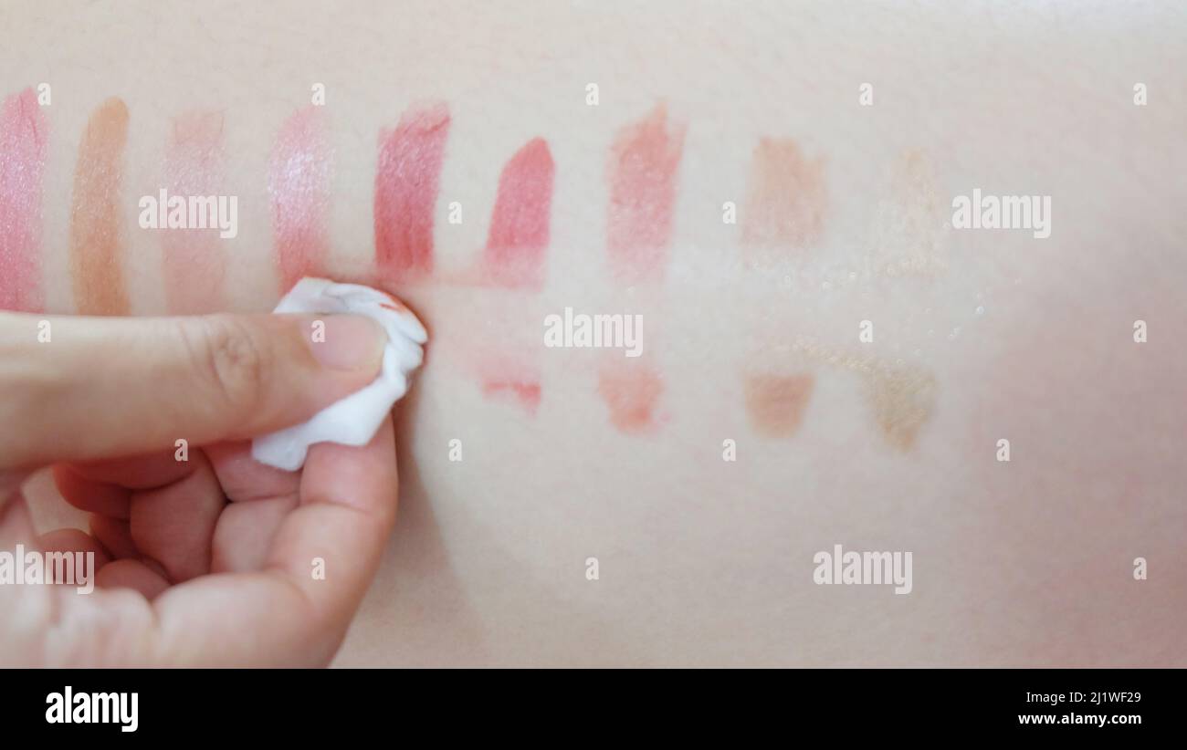 Hand wiping off lipstick patches drawn on a skin, with a piece cotton pad. Stock Photo