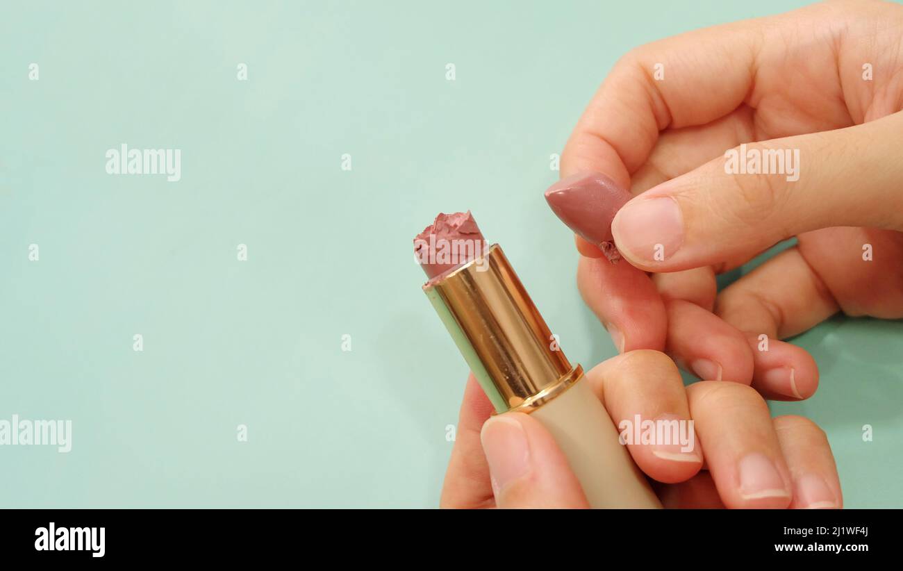Hand holding a tube of lipstick that is broken into 2 parts. With copy space on the left. Stock Photo