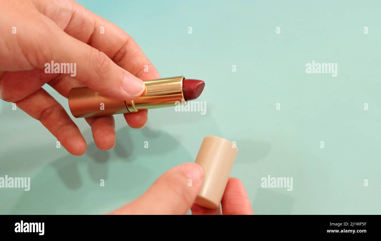Hand holding a tube of red lipstick, with the other hand holding the lid. Stock Photo