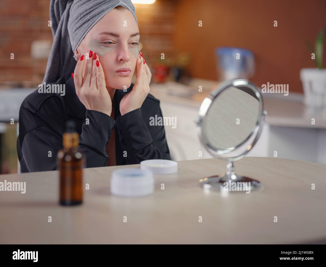 Patches for eyes. Attractive woman in kitchen with towel on her head