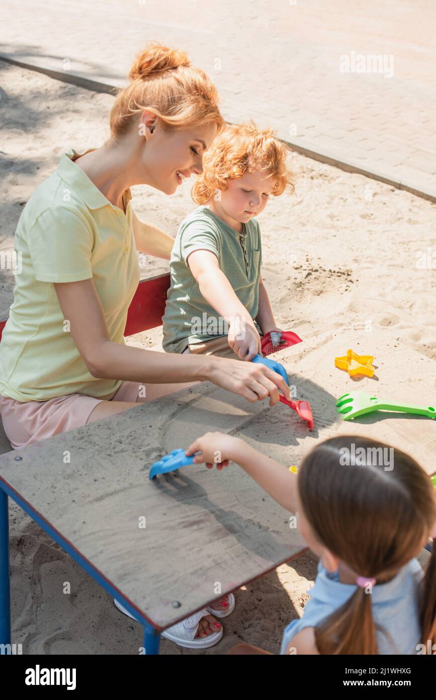 smiling woman and kids playing with toy rakes and sand outdoors Stock ...